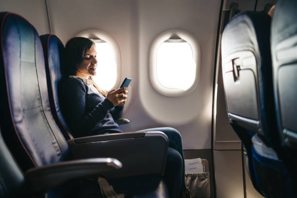 Using phone on an airplane ride Young woman is using phone on an airplane ride plane window seat stock pictures, royalty-free photos & images