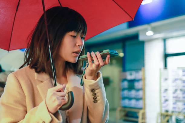 using voice recognition Asian young woman is using voice recognition on phone in the rain city speech recognition stock pictures, royalty-free photos & images