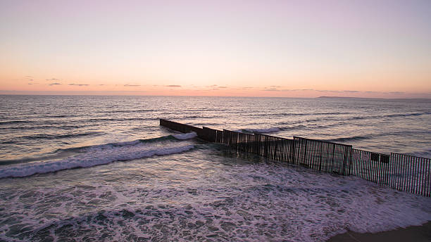 us/mexico border fence in the ocean sunset - tijuana stok fotoğraflar ve resimler
