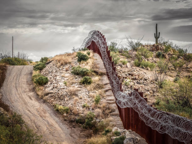 US-Mexico border wall in Sonoran Desert of Arizona with ominous skies and saguaro cactus stock photo