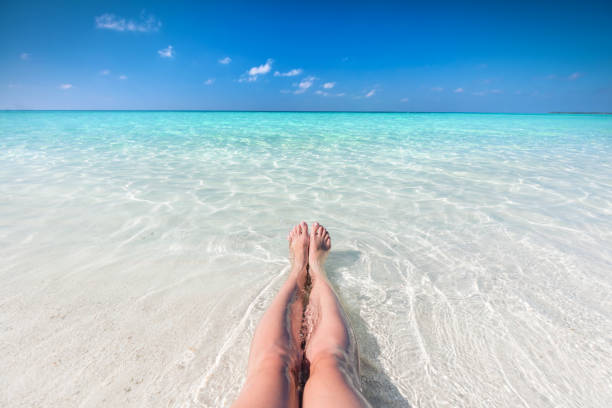 vakantie op tropisch strand in de maldiven. benen van de vrouw in de duidelijk oceaan - voeten in het zand stockfoto's en -beelden