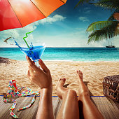 Vacation. Summer tourism. Young woman is sitting on the sand with the blue cocktail in her hand