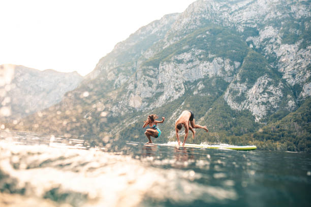 Vacationing Couple Jumping Off Paddleboard into Lake Bohinj stock photo