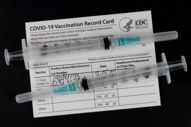 COVID-19 Vaccination Record Card with syringes or hypodermic needles. Vaccination Record Cards will be offered with each shot and a reminder for the second dose. stock photo
