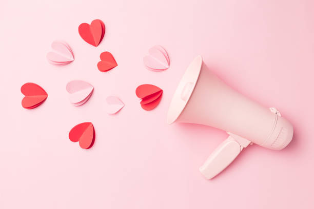 Valentine's Day background of megaphone and heart shaped confetti on pink background. stock photo