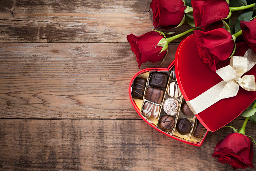 Valentine's day box of chocolates and red roses on a wood background