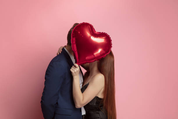 Valentine's day celebration, happy caucasian couple isolated on coral background Happy holding balloons shaped hearts. Valentine's day celebration, happy caucasian couple on coral background. Concept of human emotions, facial expression, love, relations, romantic holidays. valentines day stock pictures, royalty-free photos & images