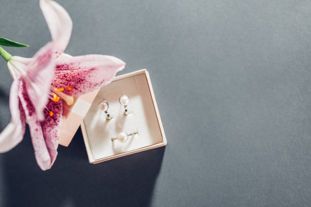 Valentines day present. Set of pearl jewellery in gift box with flowers. Earrings and ring with lily on grey background stock photo