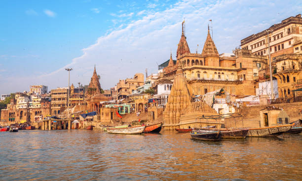 Varanasi ancient city architecture with wooden boats by the Ganges river ghat Historic Varanasi city architecture with ancient buildings and temple along the Ganges river ghat with view of wooden boat used for pleasure trips for tourists on the Ganges ganges river stock pictures, royalty-free photos & images