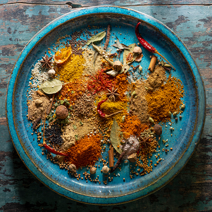 Many colorful, organic, dried, vibrant Indian food, ingredient spices are displayed on an old turquoise-colored ceramic plate background, with atmospheric lighting. Shot directly above, nice color contrast.