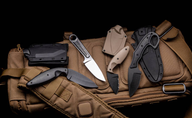 A variety of knives on a sand-colored military backpack. Dark background. stock photo