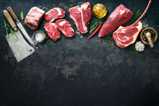 Variety of raw beef meat steaks for grilling with seasoning and utensils Variety of raw beef meat steaks for grilling with seasoning and utensils on dark rustic board cut of meat stock pictures, royalty-free photos & images