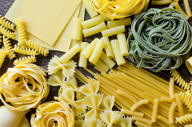 Variety of types and shapes of Italian pasta Background texture from variety of types and shapes of Italian pasta on old wooden background from above. Italian cuisine food concept and menu design. Dry pasta background. Top view. Flat lay. uncooked pasta stock pictures, royalty-free photos & images