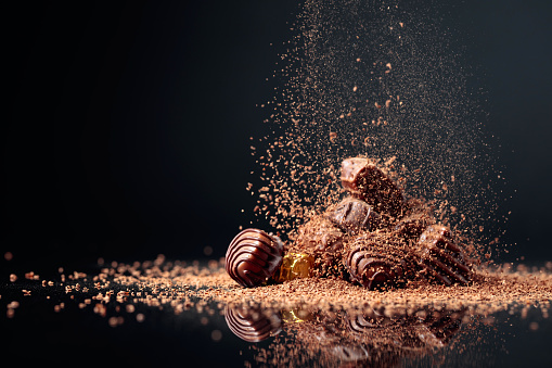 Various chocolate candies on a black background sprinkled with chocolate chips. Copy space.