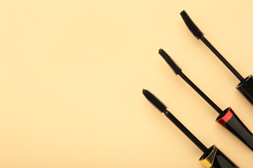 Various mascara wands on beige background with copy space. Top view