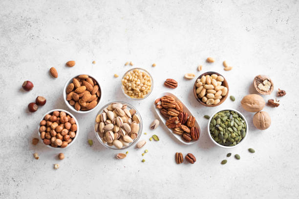 Various Nuts in  bowls Various Nuts in  bowls on white background, top view, copy space. Nuts assortment - pecans, hazelnuts, walnuts, pistachios, almonds, pine nuts, peanuts, pumpkin seeds. seed stock pictures, royalty-free photos & images