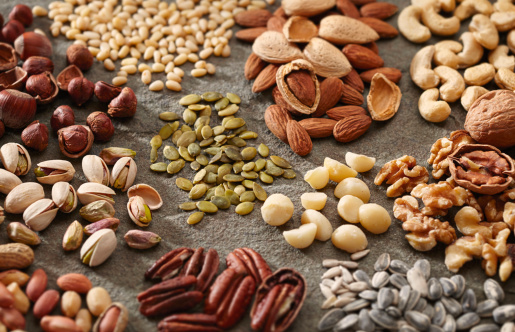 A variety of healthy and organic nuts and seeds in piles on a slate surface.
