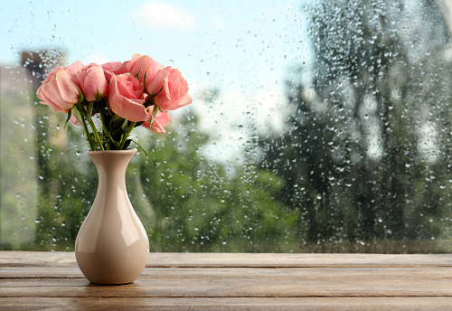 Vase with roses near window on rainy day. Space for text