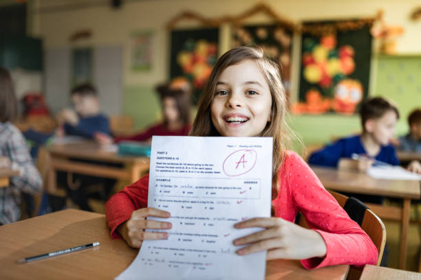 I've got an A on my exam! Happy schoolgirl showing her A grade on a test at elementary school and looking at camera. students exam results stock pictures, royalty-free photos & images