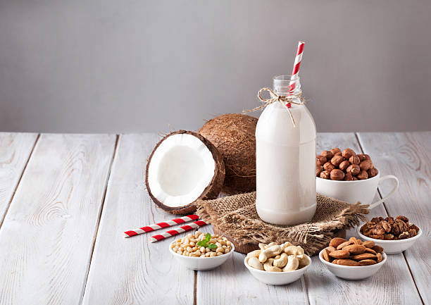 Vegan nut milk in the bottle Vegan milk from nuts in the bottle with red stripped straw around various nuts on white wooden table coconut milk stock pictures, royalty-free photos & images