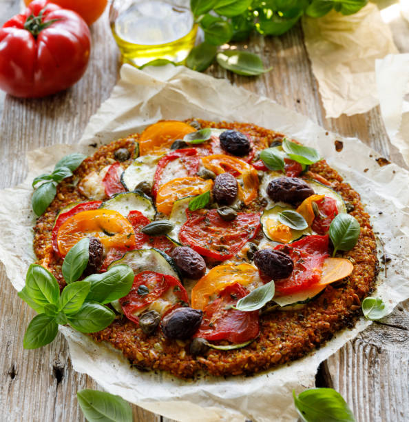 Vegan pizza on a carrot base with tomatoes, zucchini and olives sprinkled with fresh basil, close up view. Healthy food idea stock photo
