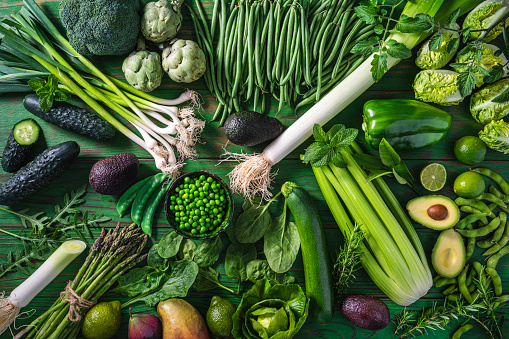Vegan raw vegetables on green wooden table full frame background