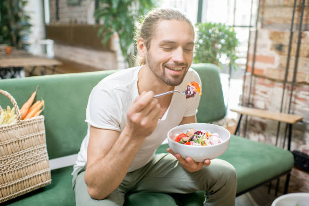 vegetarische mann isst salat im innenbereich - essen mund benutzen stock-fotos und bilder