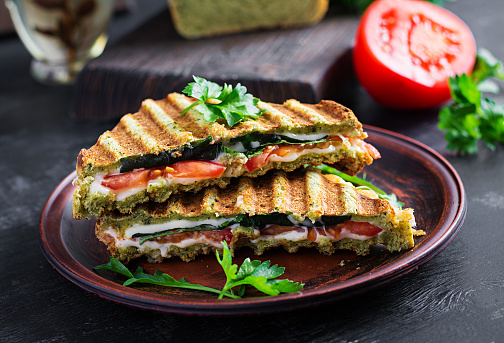 Vegetarian sandwich panini with spinach leaves, tomatoes and cheese on a dark table. Toast with cheese.