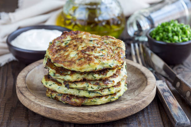 Vegetarian zucchini fritters or pancakes, served with greek yogurt and green onion on wooden background, horizontal stock photo