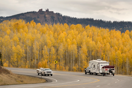 Vehicles drives past the glowing yellow aspen trees below the Rabbit Ears Peak rock formation on the continental divide off Highway 40 and Rabbit Ears Pass outside Steamboat Colorado.