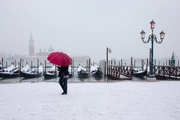Venice in snow: woman with red umbrella with gondolas on St. Mark square stock photo