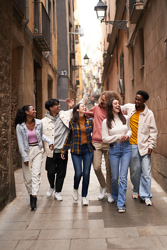 Vertical photo of a group of young happy friends walking in the street of the city. Smiling students laughing and having fun togethers. High quality photo
