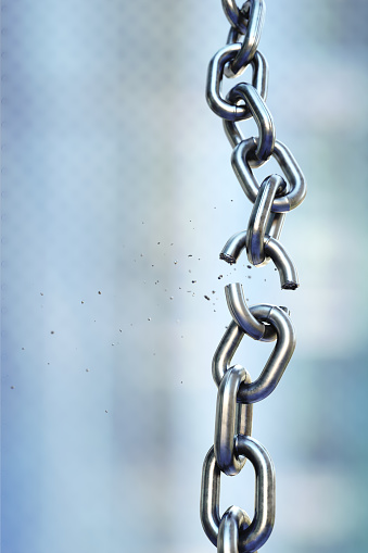 A vertical shiny chain with a link in the process of breaking, isolated on a defocused blue background. Vertical composition.