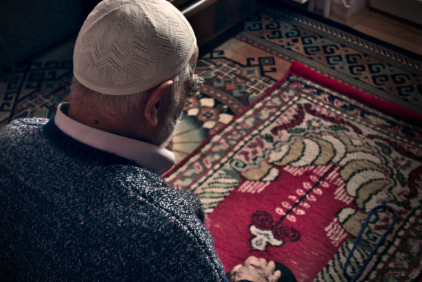 Very old Turkish muslim man doing Salah prayer at his home on his prayer rug Very old bearded Turkish muslim male at his 80's wearing a prayer cap doing Salah prayer at his home on his prayer rug in Ramadan month old man muslim  pray stock pictures, royalty-free photos & images