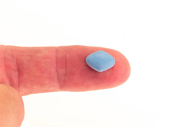Viagra anti-impotence tablet on a patients finger A blue anti-impotence tablet on a patients finger - studio shot with a white background anti impotence tablet stock pictures, royalty-free photos & images