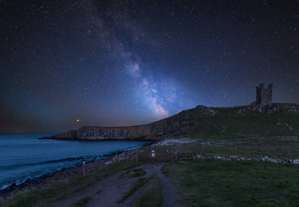 Vibrant Milky Way composite image over landscape of Dunstanburgh Castle on Northumberland coastline in England stock photo