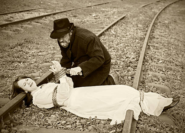 victorian-vignette-of-villain-tying-maiden-to-railroad-picture-id108351486