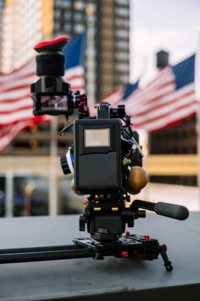 Video camera ready for shoot Modern professional 4K video camera on camera slider against the  view of modern cityspace with American flags and office buildings. michigan shooting stock pictures, royalty-free photos & images