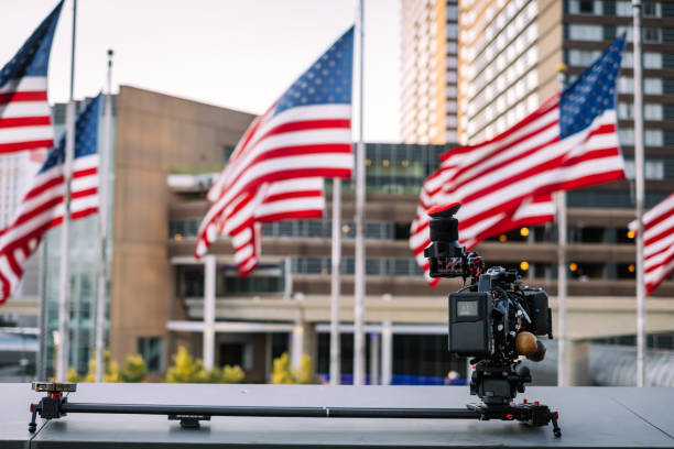 Video camera ready for shoot Modern professional 4K video camera on camera slider against the  view of modern cityspace with American flags and office buildings. michigan shooting stock pictures, royalty-free photos & images