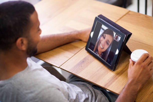 Video conference call with the girlfriend Afro american male on the digital tablet conference call. Young woman on the other side. Sitting in coffe shop with cup of coffee. long distance relationship stock pictures, royalty-free photos & images