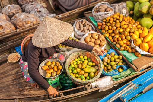 Vietnamese fruits seller on floating market - woman selling fruit from her boat in the Mekong river delta, Vietnam.