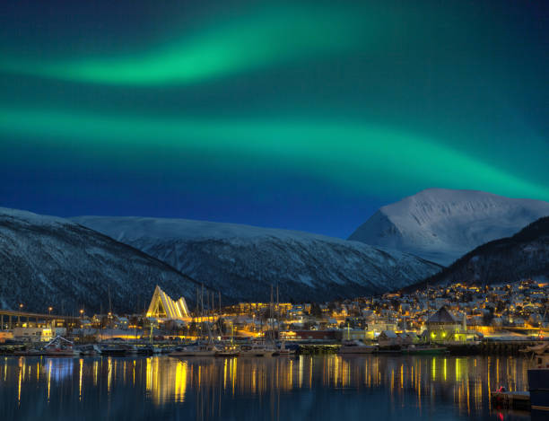 View at night on illuminated Tromso city with cathedral and majestic aurora borealis stock photo