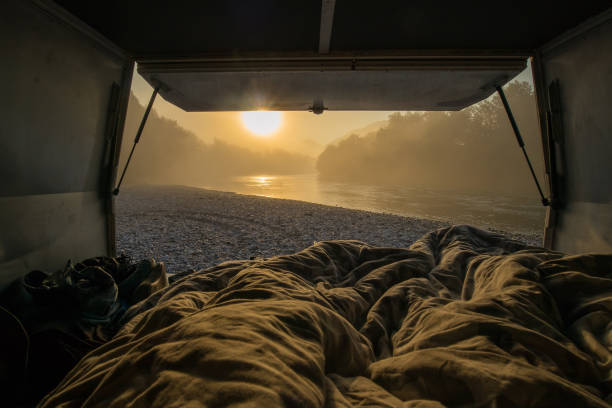 View from a bed in the vintage campervan parked on the shores of a river in early morning hours. Romantic overnight stay at a wild camping next to a river. stock photo