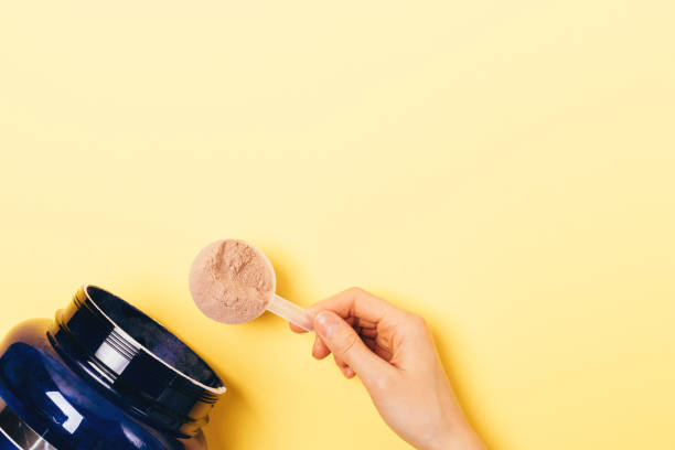 View from above female hand takes spoonful View from above female hand takes spoonful of protein powder from jar on yellow background with copy space. protein stock pictures, royalty-free photos & images