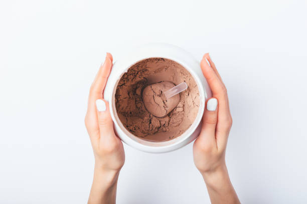 View from above female's hands holding View from above female's hands holding open container of chocolate protein powder on white table. protein stock pictures, royalty-free photos & images