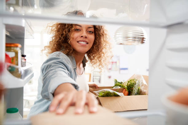 女性がオンラインホームフード配達を解凍するように冷蔵庫の中から外を見る - 冷蔵庫　中 ストックフォトと画像