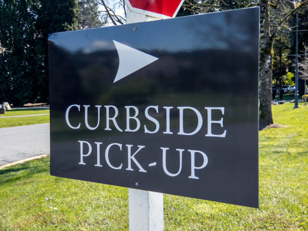 view of a curbside pickup sign in the grass outside a large business property during coronavirus Angled view of a curbside pickup sign in the grass outside a large business property during coronavirus curbsidepickup stock pictures, royalty-free photos & images
