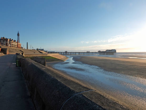 view of blackpool tower and north pier from the promenade with town buildings in afternoon sunlight view of blackpool tower and north pier from the promenade with town buildings in afternoon sunlight north pier stock pictures, royalty-free photos & images
