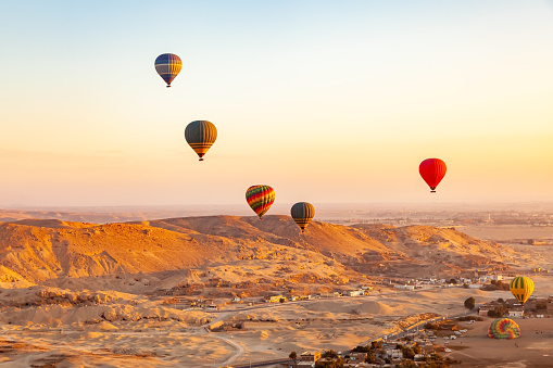 View of colorful hot air balloons flying over Valley of The Kings in the morning and some of them landing on the plane near the village.