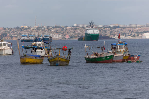 View of fishing boats on the coast of Luanda city, Luanda Bay, with Port of Luanda, transport ships and containers in the background, Angola stock photo
